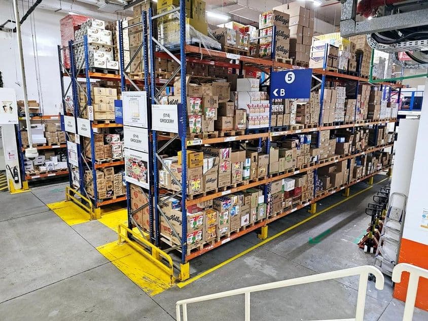 Depósito com sistemas de prateleiras, categorias de produtos rotuladas e sinalizações de segurança auxiliando operações tranquilas.