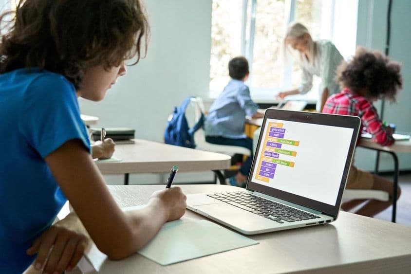Estudante do ensino médio usando laptop para inserir dados de programação.