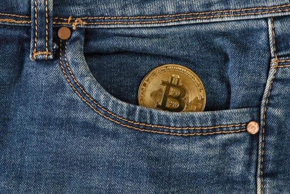 Uma moeda de bitcoin dourada está em um bolso de jeans.