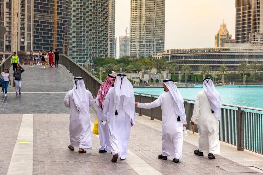Homens árabes em traje branco tradicional caminhando no centro de Dubai.