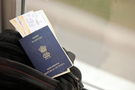 Passaporte indiano azul com passagens aéreas em uma mochila de viagem.