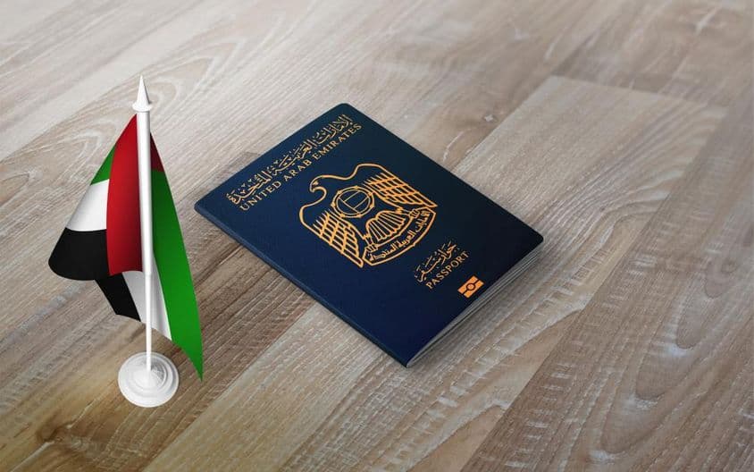 Passaporte dos Emirados Árabes Unidos sobre uma superfície de madeira, com uma bandeira nacional.