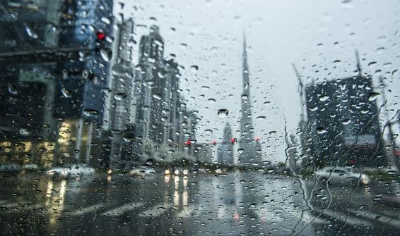 Chuva em Dubai, paisagem urbana desfocada ao fundo.
