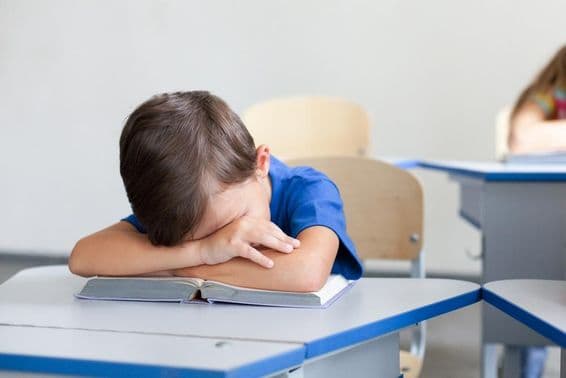Criança escolar dormindo durante uma aula entediante.