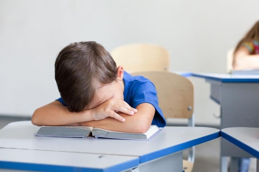 Criança escolar dormindo durante uma aula entediante.