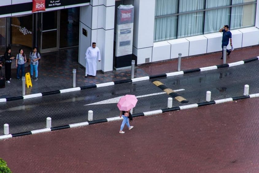 Uma menina com um guarda-chuva caminhando na chuva na cidade de Dubai.
