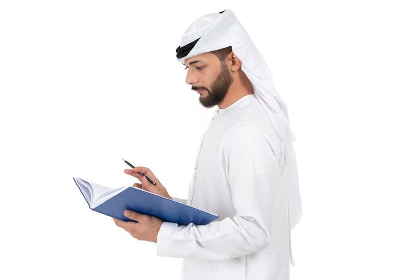 Professor árabe jovem em pé e escrevendo no livro.