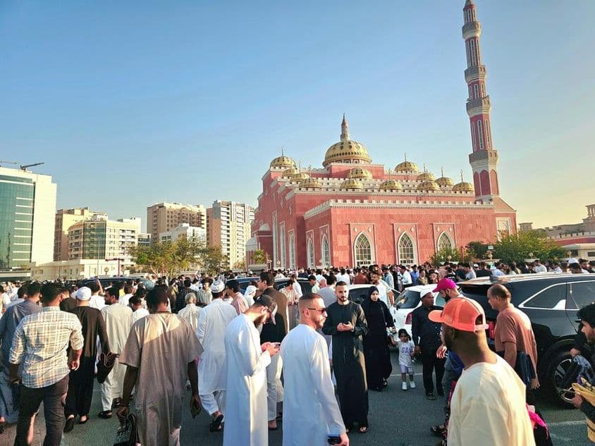 Uma grande multidão reunida em frente a uma grandiosa mesquita com cúpulas e altos minaretes.