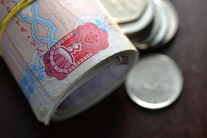 Dirhams dos EAU enrolados acompanhados de algumas moedas.