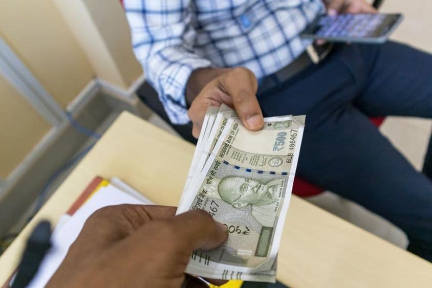 Uma pessoa entregando uma nota de 500 rupias indianas para outra pessoa.