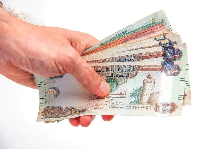Um homem segurando notas de dirham dos Emirados Árabes Unidos.