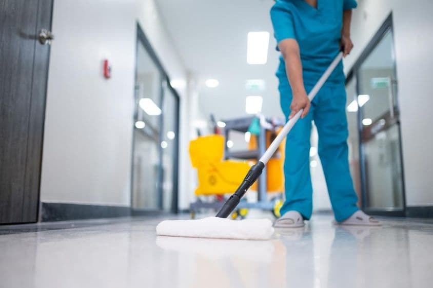 Faxineiro passando pano no chão do corredor.