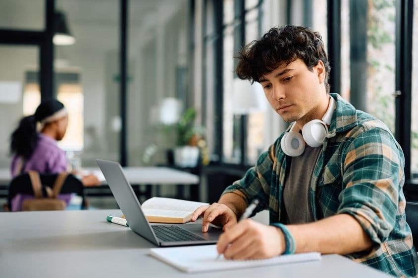 Estudante universitário usando um laptop enquanto escreve.