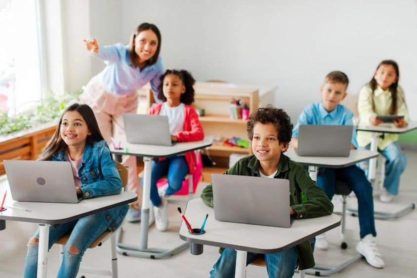 Grupo de crianças recebendo aula usando laptops.