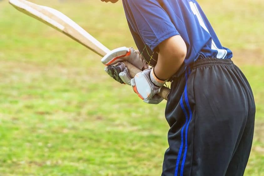 Jovem asiática jogadora de críquete em equipamento de proteção acertando uma bola com um bastão em campo.