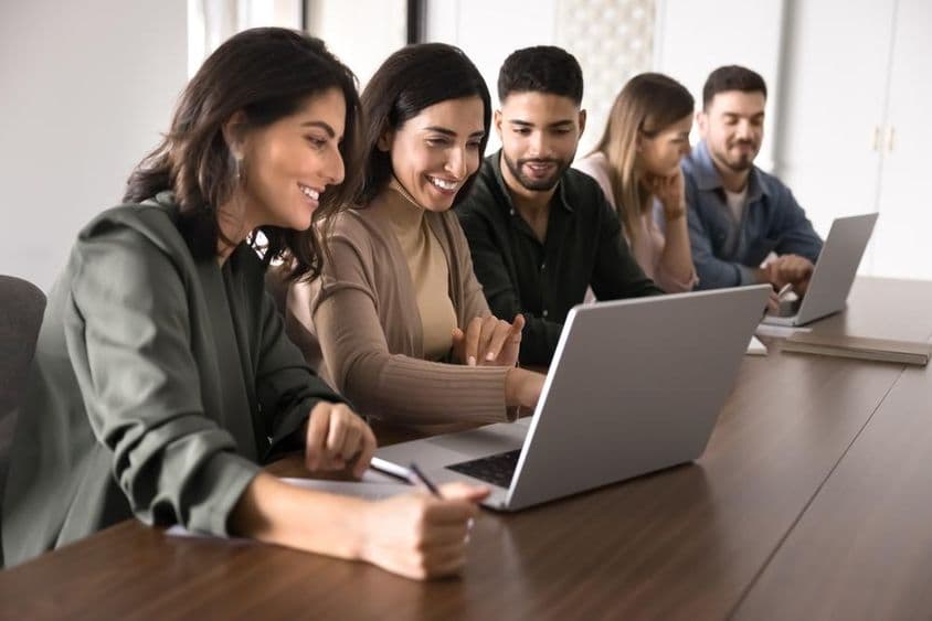 Estudantes jovens de várias nacionalidades estudando em laptops em um centro educacional.