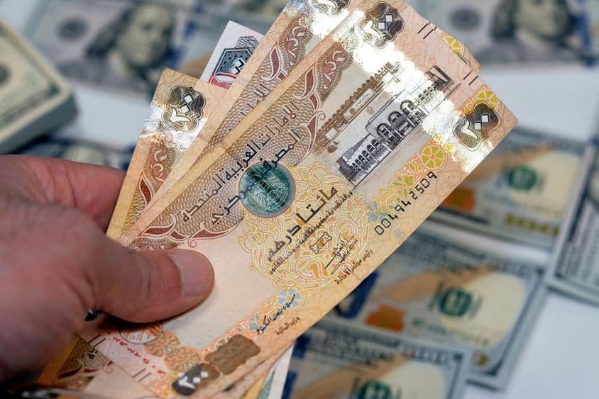 Um homem segurando um maço de notas de 200 dirhams dos Emirados Árabes Unidos.
