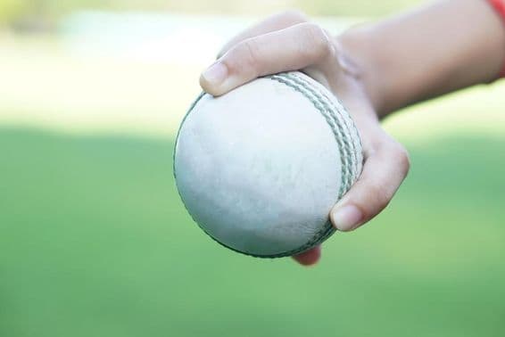 Um jogador de críquete segurando uma bola de críquete de couro branca.