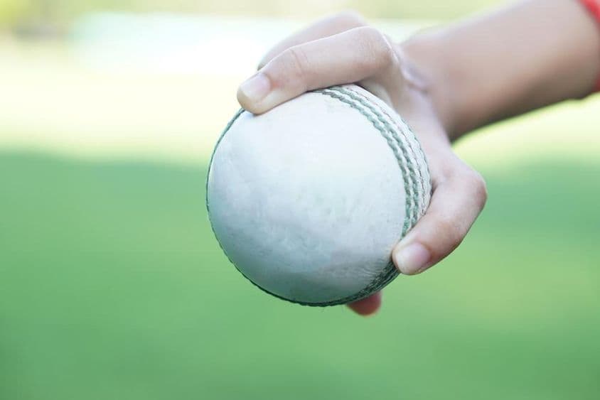 Um jogador de críquete segurando uma bola de críquete de couro branca.