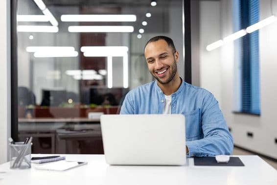 Um jovem profissional feliz sorrindo enquanto trabalha em um computador.
