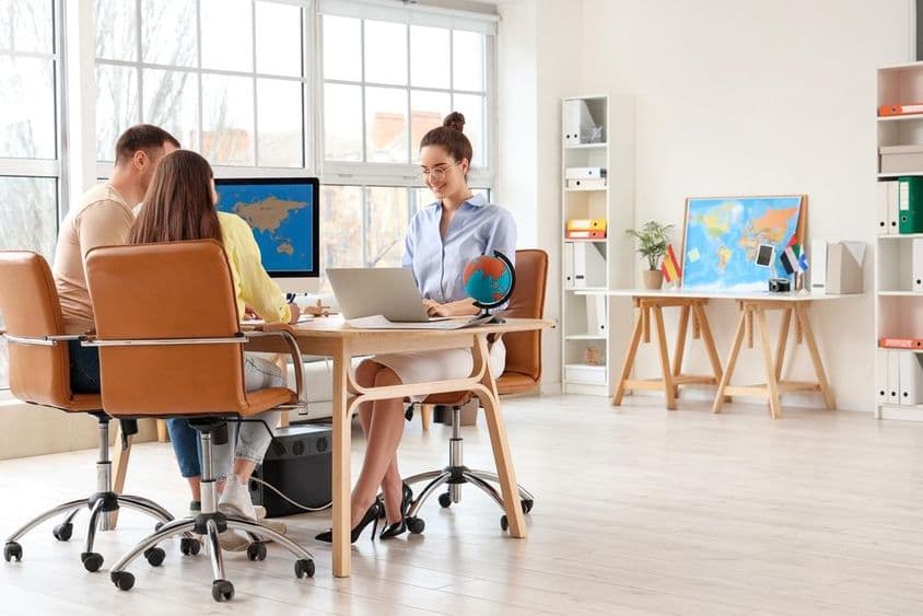 Agente de viagens trabalhando em um laptop com um casal jovem na mesa em um escritório.