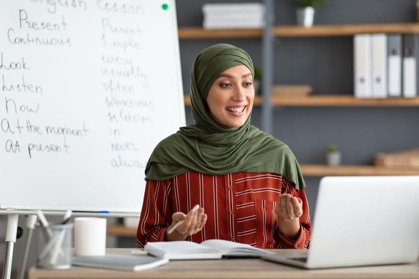 Professora árabe sorridente de hijab iniciando chamada de vídeo.
