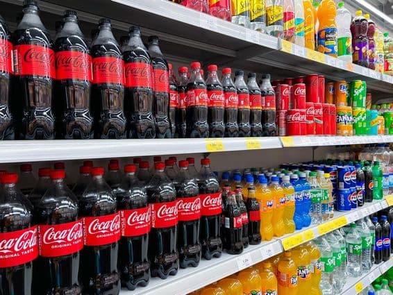 Fila de garrafas de cola em uma prateleira de supermercado.