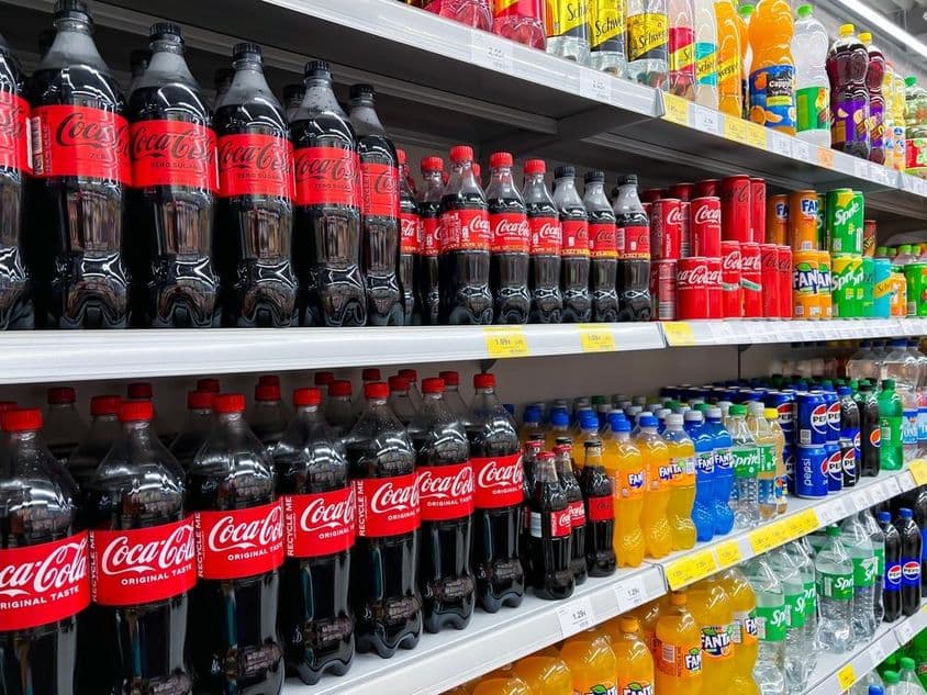 Fila de garrafas de cola em uma prateleira de supermercado.