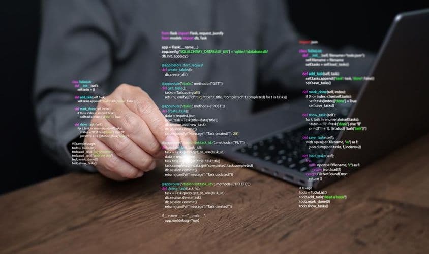 Mãos de um programador em um laptop com codificação.