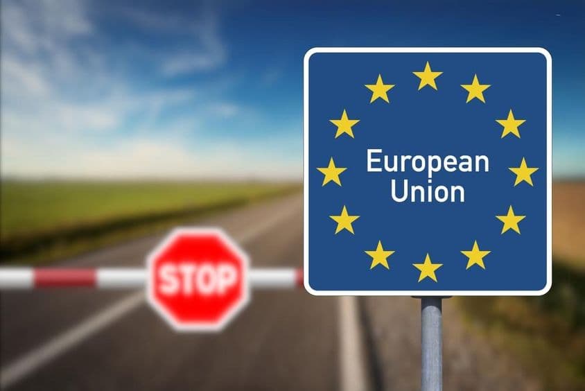 Emblema da União Europeia e uma passagem de fronteira com barreira e placa de pare.