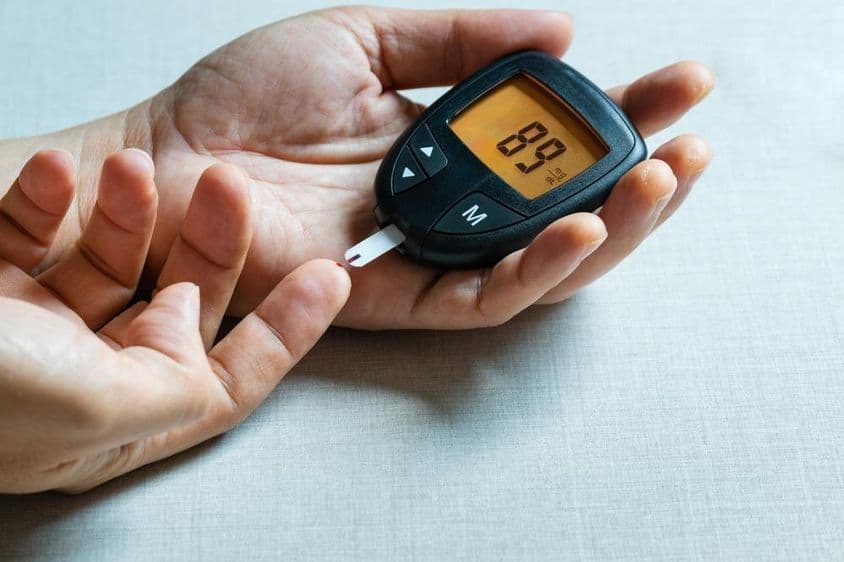 Mãos de um homem usando um medidor digital de glicose no sangue para monitorar diabetes.