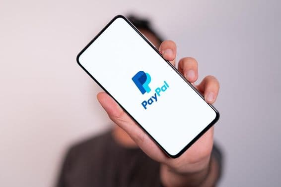 Um homem segurando um telefone com o logotipo do PayPal visível na tela do telefone.