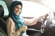 Mulher árabe feliz de hijab dirigindo seu carro com um sinal de positivo.