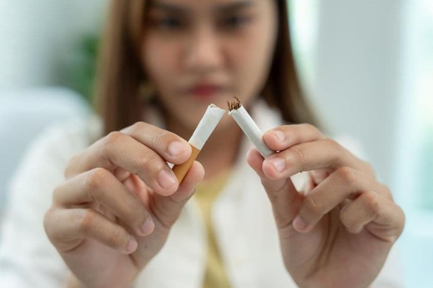 Proibição de fumar, uma mulher quebra um cigarro ao meio.