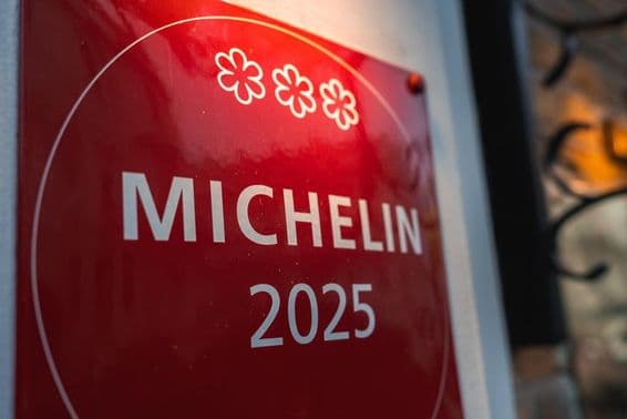 Uma placa vermelha de três estrelas Michelin 2025 em uma parede de cor clara.