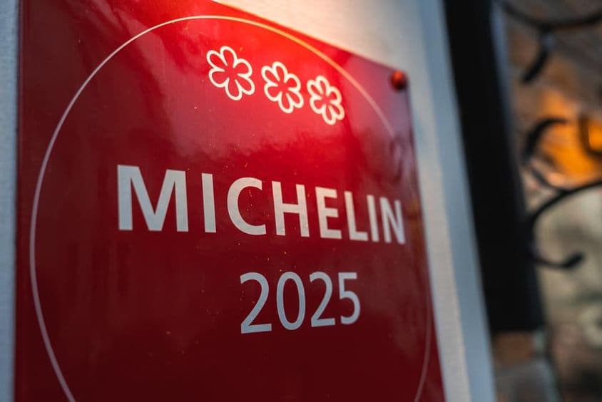 Uma placa vermelha de três estrelas Michelin 2025 em uma parede de cor clara.