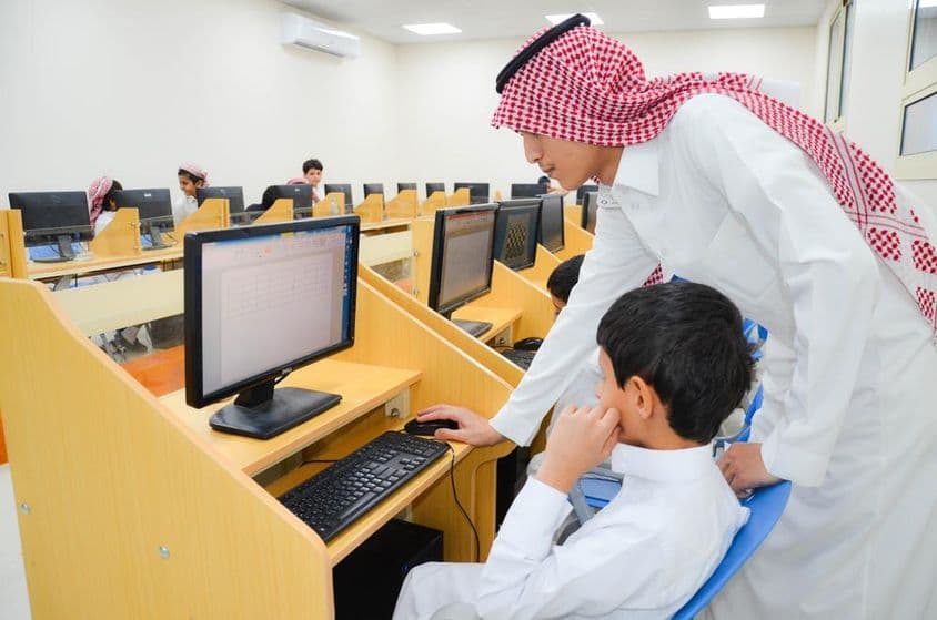 Em um laboratório de educação em informática, uma professora instrui os alunos sobre o uso de computadores.