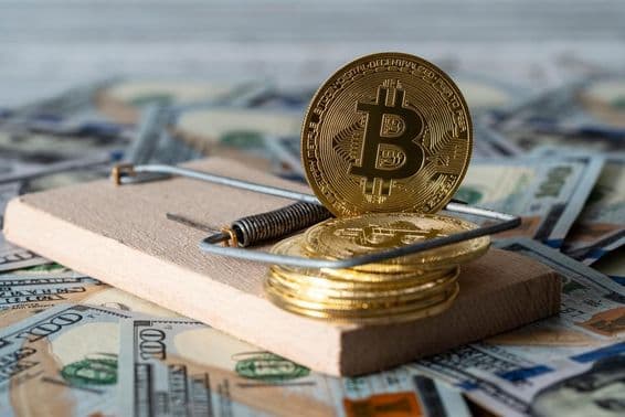 Moedas de criptomoeda douradas bitcoin em uma armadilha de rato, com notas de 100 dólares dos EUA ao fundo.