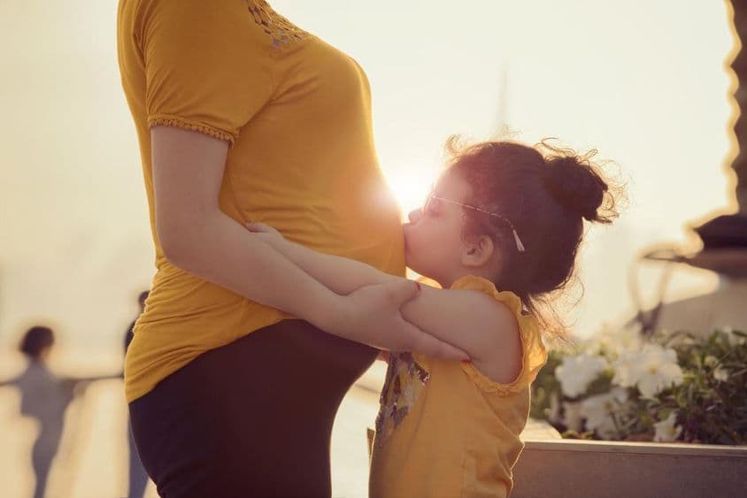 Criança beijando a barriga da mãe.
