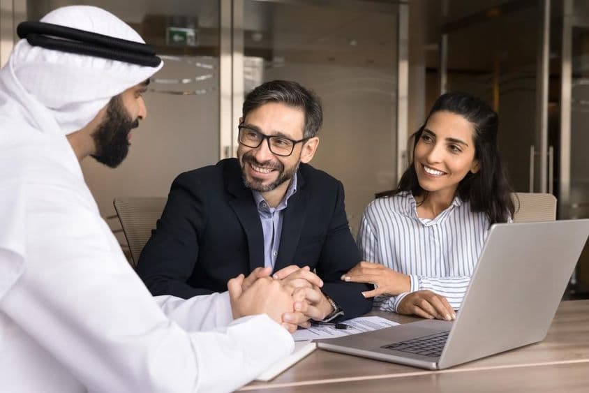 Um casal latino feliz se reunindo com um agente imobiliário árabe.