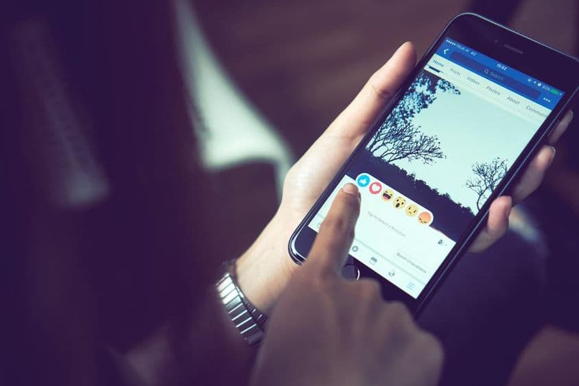 Uma mão pressionando Facebook em um Apple iPhone 6.