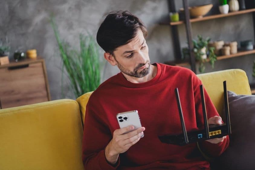 Um jovem relaxando em casa com um smartphone e roteador, desfrutando de uma tarde tranquila.