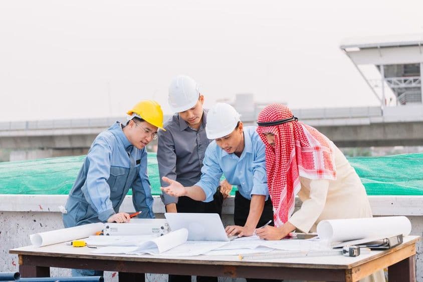 Empresário árabe, engenheiro e trabalhador analisam planos de construção utilizando um laptop.