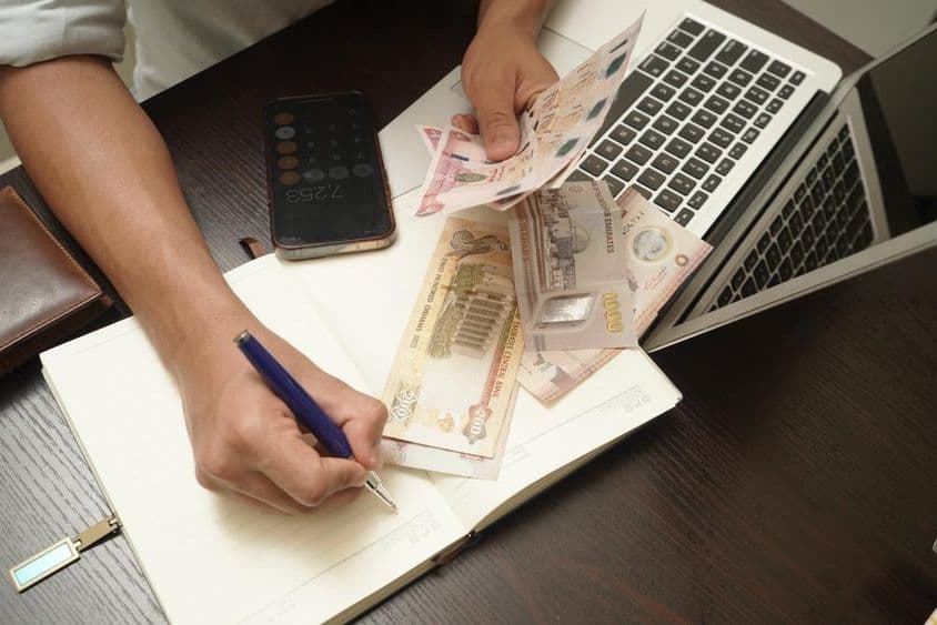 Um homem sentado em uma mesa contando um maço de notas de dirham dos EAU.