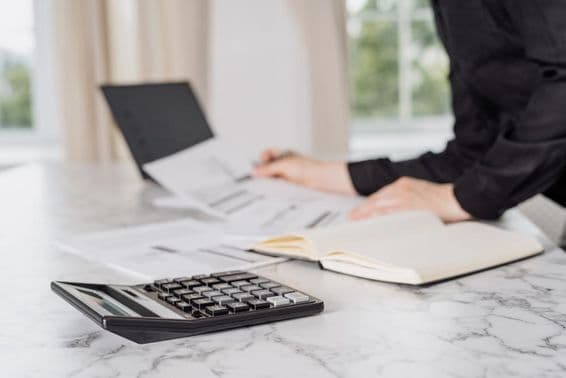 Uma mulher vestindo roupas pretas calculando despesas com um laptop.