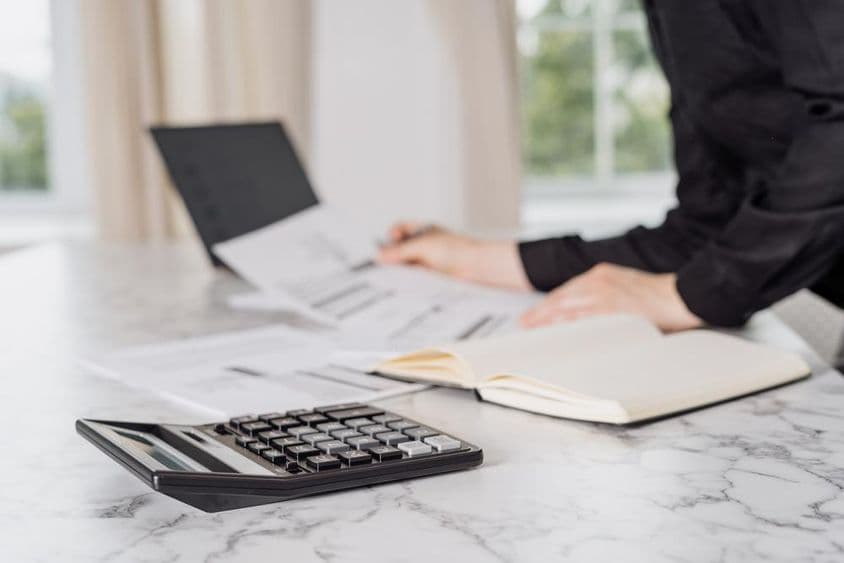 Uma mulher vestindo roupas pretas calculando despesas com um laptop.