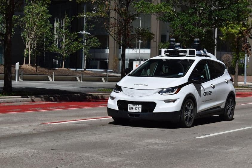 Um carro autônomo branco supervisionado a cruzar no distrito financeiro do centro.