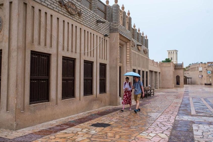 Um casal de turistas caminhando sob um guarda-chuva nas ruas de Dubai.