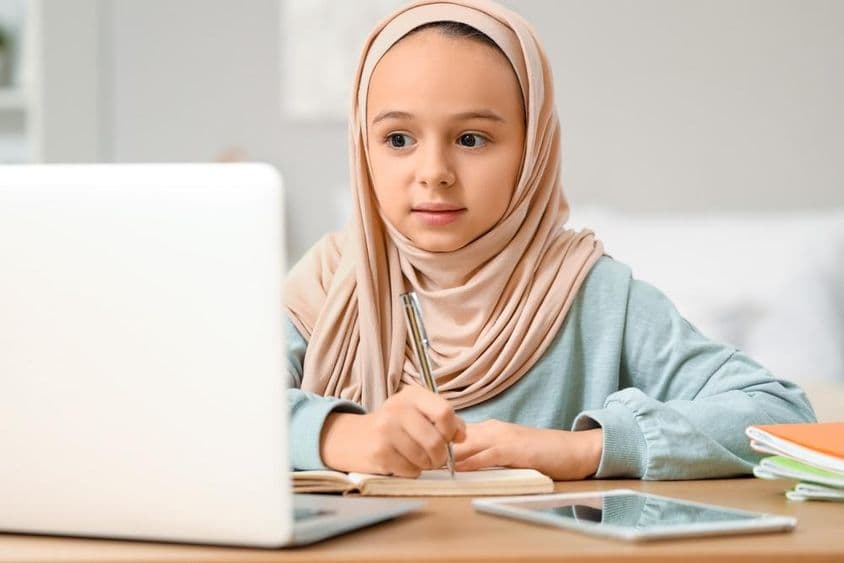 Menina muçulmana pequena de hijab fazendo lição de casa em casa.