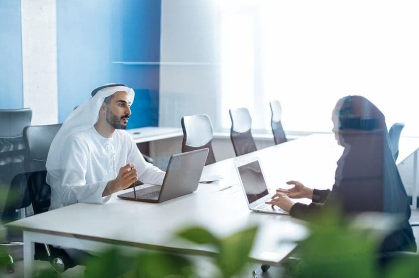 Homem e mulher em trajes tradicionais trabalhando em um escritório de negócios em Dubai.